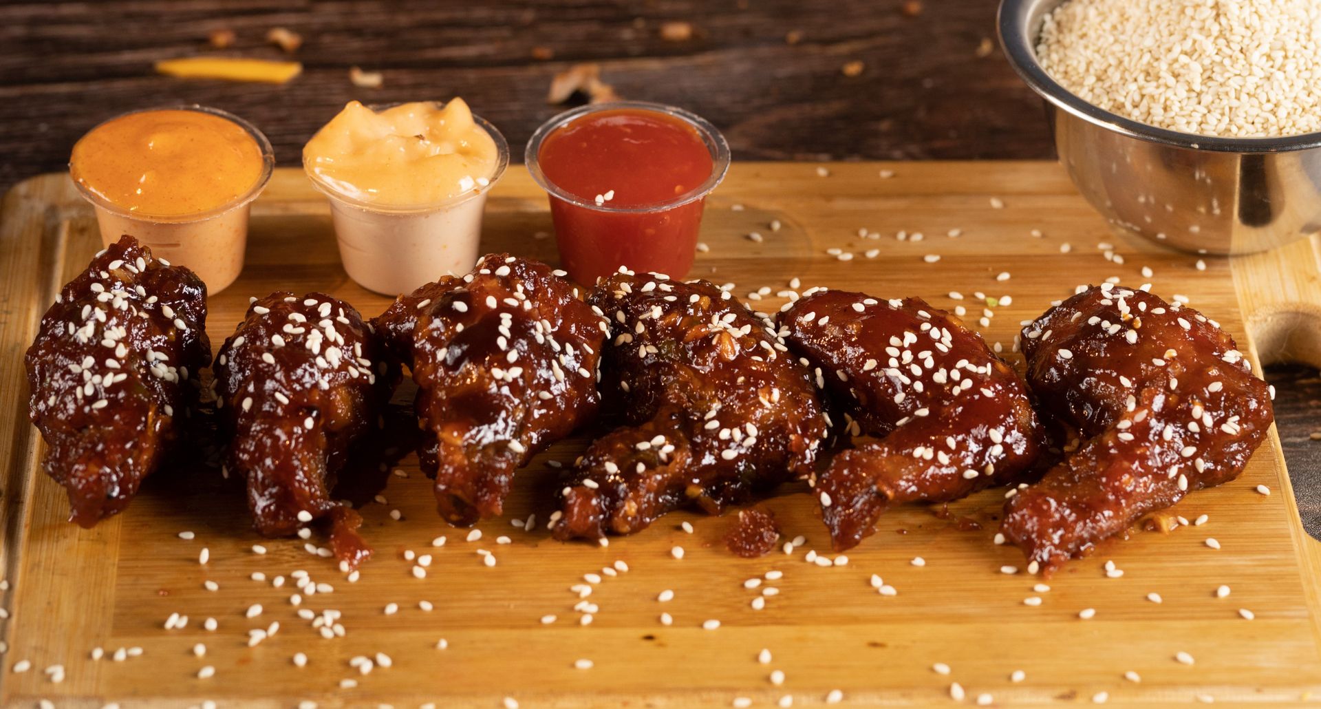 Baskets of chicken wings in many different sauces across a dark table with sauce bowls