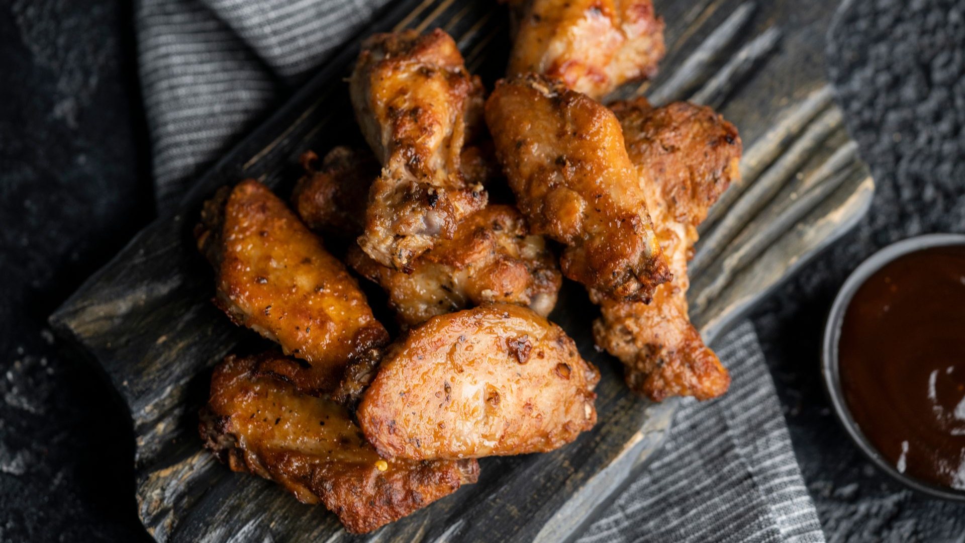 Crispy golden chicken wings piled on a dark wooden board with dipping sauce