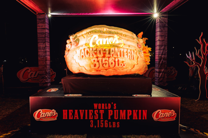 The 3,156 pound carved pumpkin lit up at night on a display pedestal in Salem, with World's Heaviest Pumpkin 3,156 lbs written on the stand