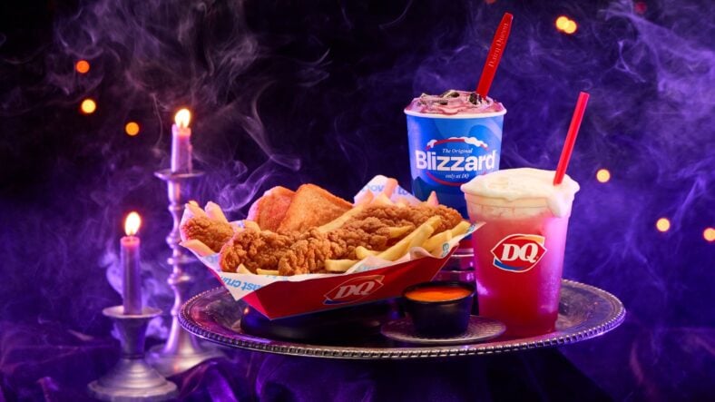 A Dairy Queen promotional photo of the Spellbound Series on a tray: a chicken strip basket with fries and a cup of orange sauce, an Enchanted OREO Blizzard cup, and a pink Bubble Brew DQ Sparkler with cold foam, against purple smoke and candles
