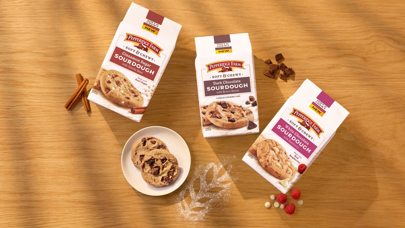 Three bags of Pepperidge Farm Sourdough Cookies in Cinnamon Sugar, Dark Chocolate, and White Chocolate flavors on a wood table with cinnamon sticks, chocolate chunks, raspberries, and a plate of cookies