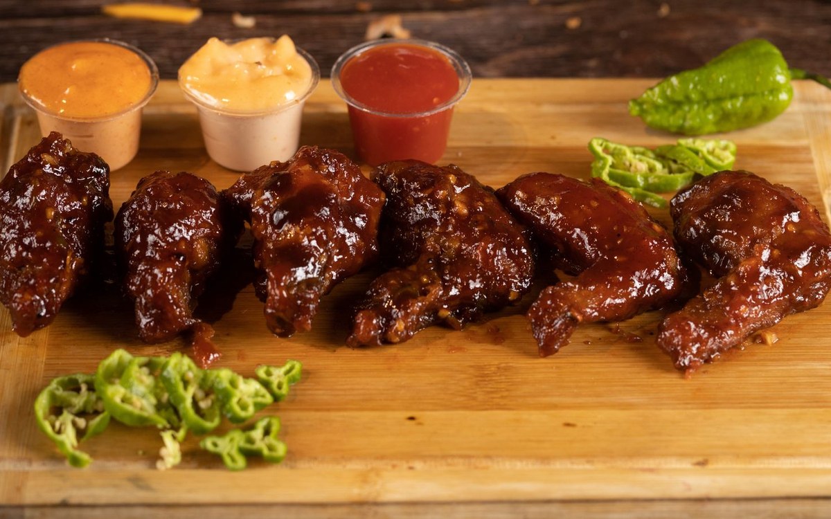 A wooden board of glazed chicken wings with dipping sauces