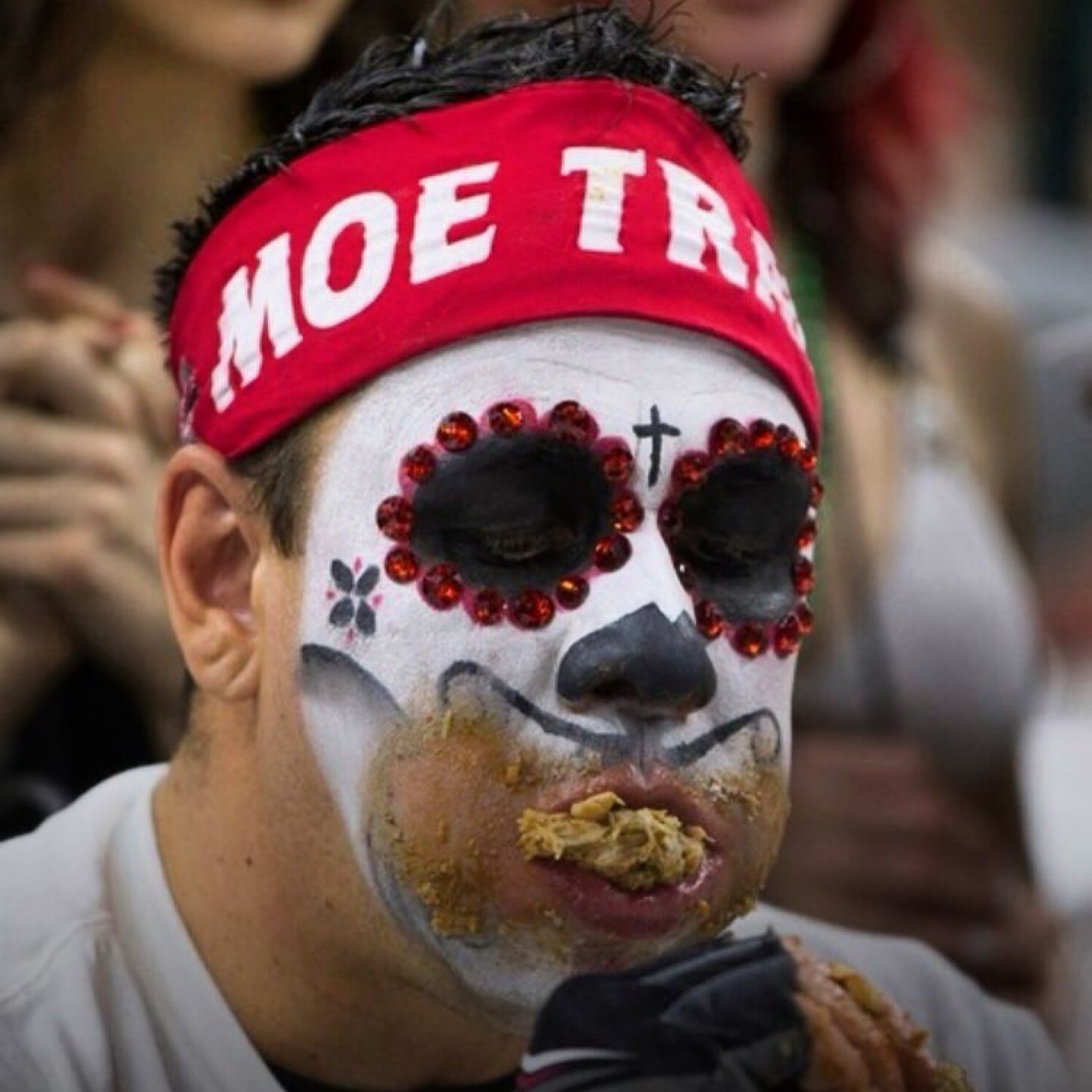 Moe Train in full Wing Bowl face paint mid-bite, wing meat in his mouth and sauce across his chin