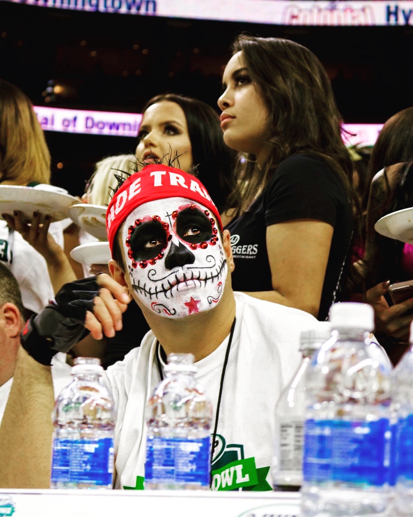 Moe Train at the Wing Bowl table in face paint, looking up as fresh plates of wings pass behind him