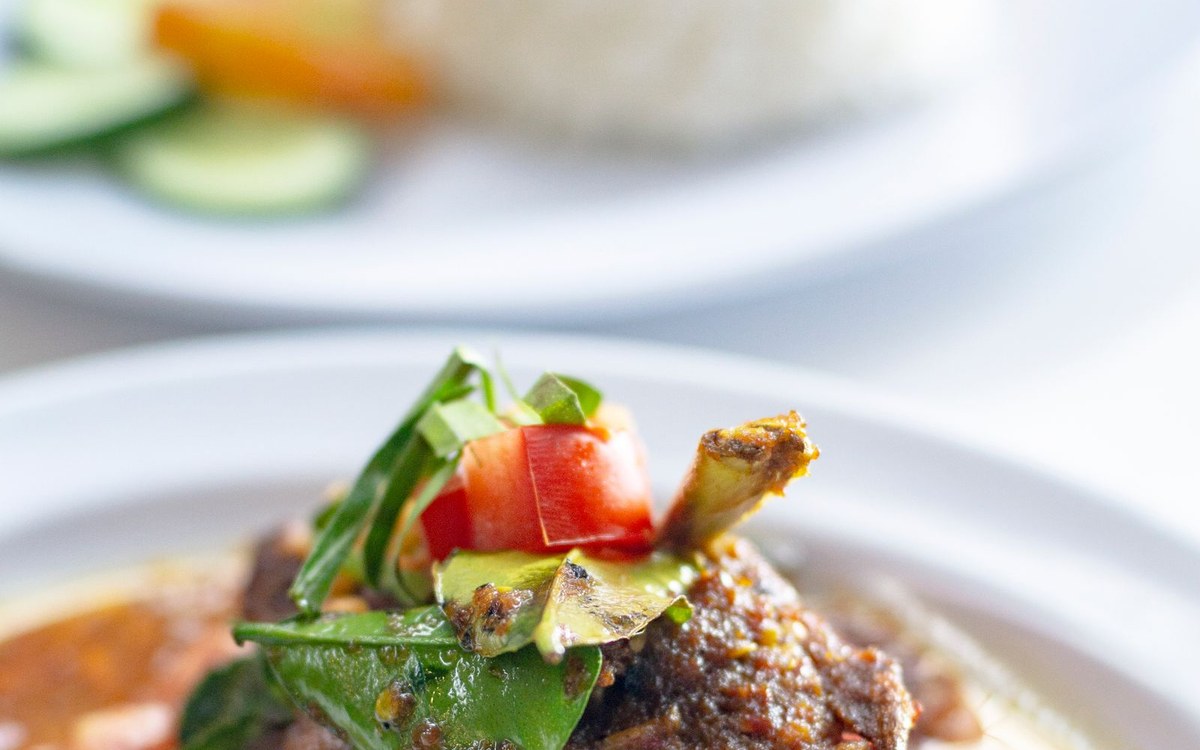 Dark braised beef rendang topped with herbs, with rice in the background