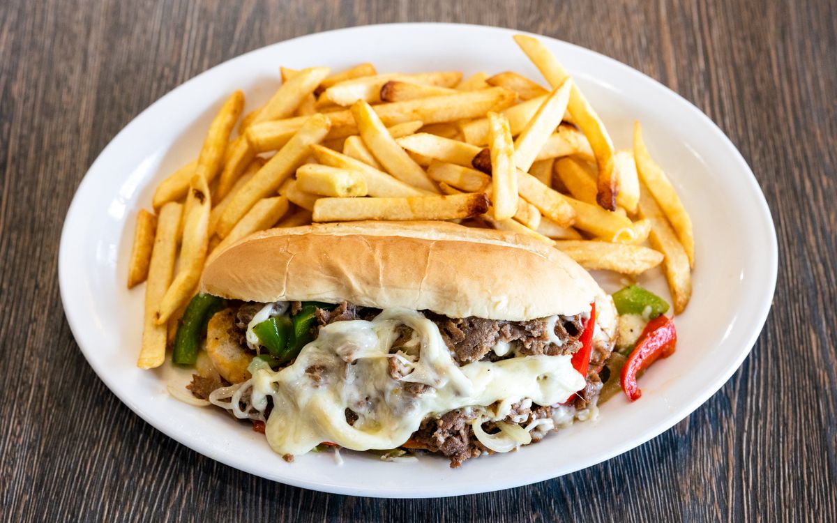 A cheesesteak sandwich with melted cheese, peppers, and a side of fries