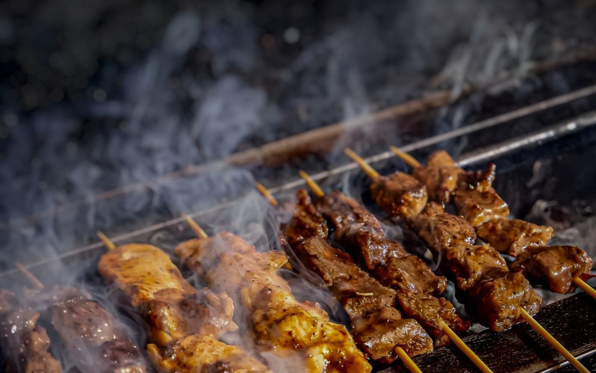 Chicken satay skewers grilling over charcoal with smoke rising