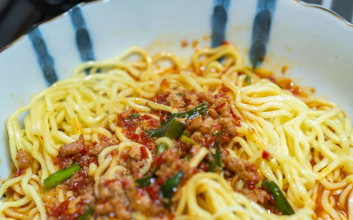 A bowl of wheat noodles topped with minced pork in red chili sauce and chopped green onions