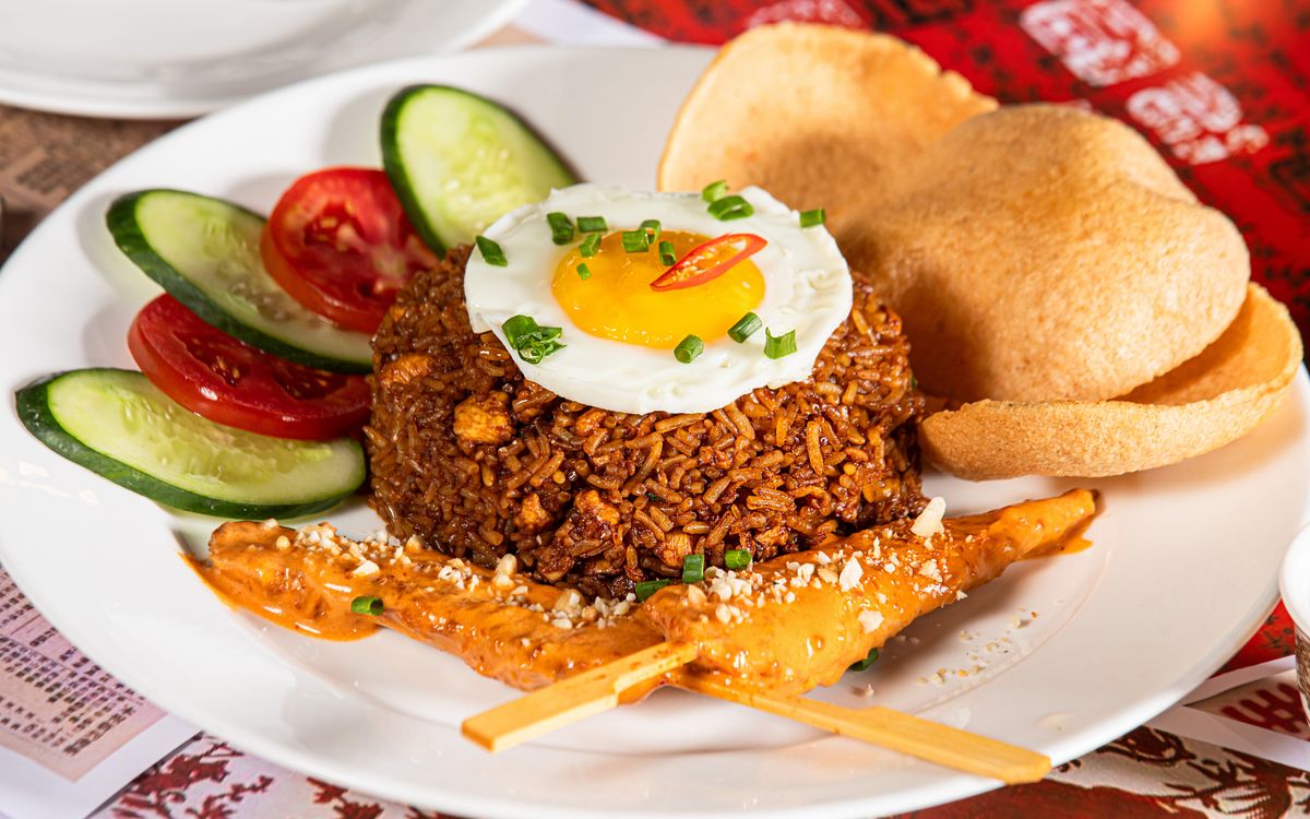 Nasi goreng fried rice topped with a fried egg, with satay and crackers on the side