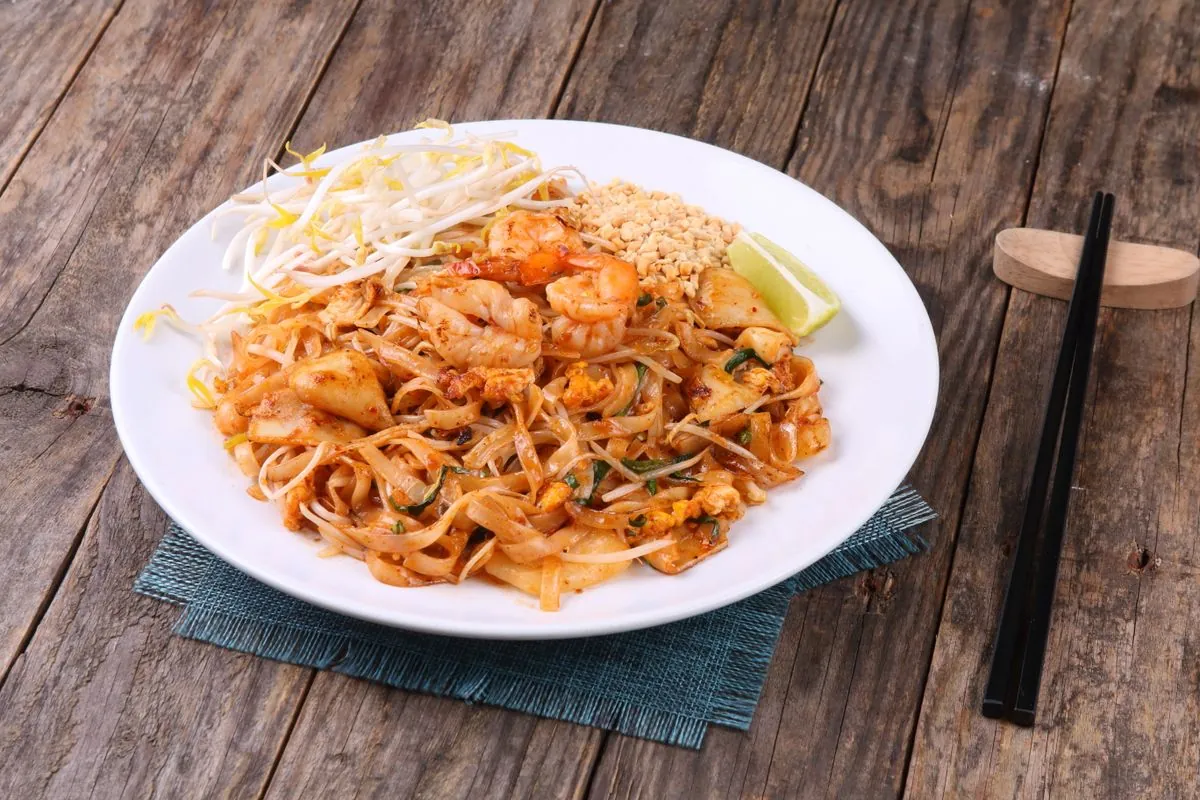 A plate of pad thai with shrimp, flat rice noodles, crushed peanuts, bean sprouts, and a lime wedge