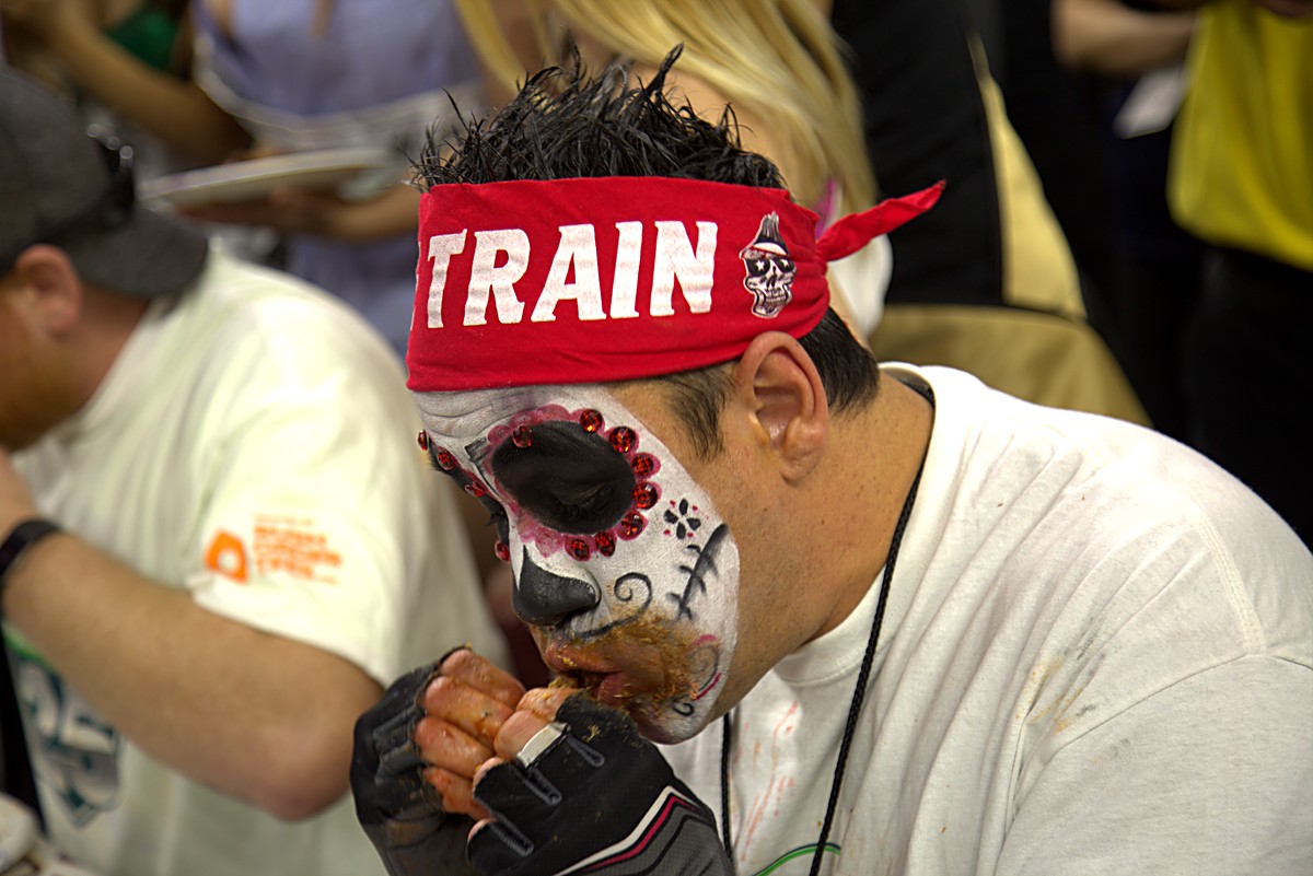 Close profile of an eater in a red headband mid-bite at the competition table at Wing Bowl 25