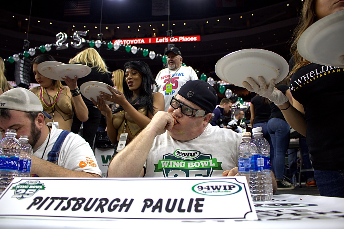 Competition table with plates of wings carried overhead and balloons above at Wing Bowl 25