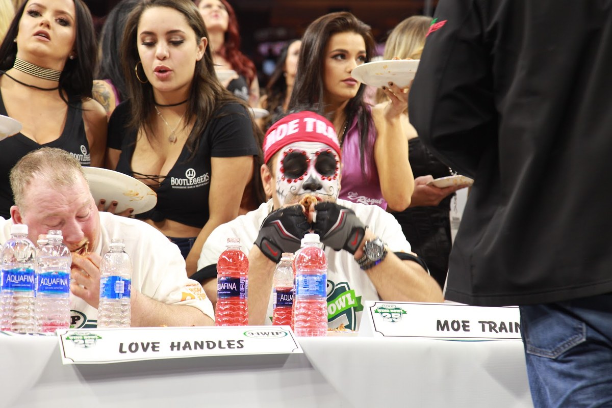 Moe Train at the Wing Bowl 25 table in skull face paint and his red MOE TRAIN headband, eating mid-contest with his name plate on the table in front of him